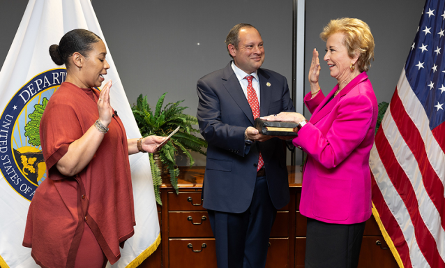 A woman in a pink blazer, Linda McMahon, holds her hand up during a swearing in ceremony.