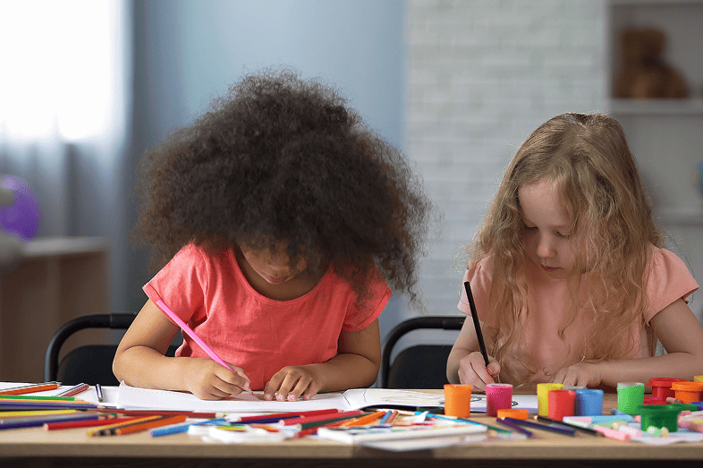Two multi-racial girls drawing with colorful pencils in early education center