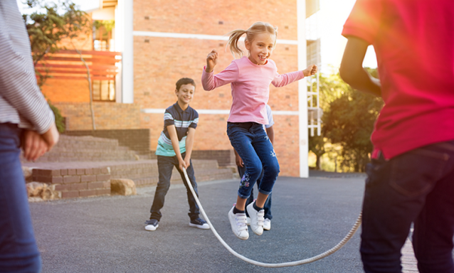 Happy cute girl jumping over skipping rope held by her friends.
